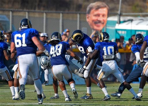 A member of the Dallas Cowboys is thrown to the ground by St. Louis Rams tight end Jared Cook, center, during a scuffle as fans hold up a picture of Rams owner Stan Kroenke during a joint NFL football training camp, Tuesday, Aug. 18, 2015, in Oxnard, Calif. (AP Photo/Mark J. Terrill)