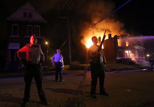Police stand guard as firefighters extinguish a vacant house that was set on fire during protests following a fatal officer-involved shooting Wednesday, Aug. 19, 2015, in St. Louis. A black 18-year-old fleeing from officers serving a search warrant at a home in a crime-troubled section of St. Louis was fatally shot Wednesday by police after he pointed a gun at them, the city's police chief said. (Laurie Skrivan/St. Louis Post-Dispatch via AP) EDWARDSVILLE INTELLIGENCER OUT; THE ALTON TELEGRAPH OUT; MANDATORY CREDIT