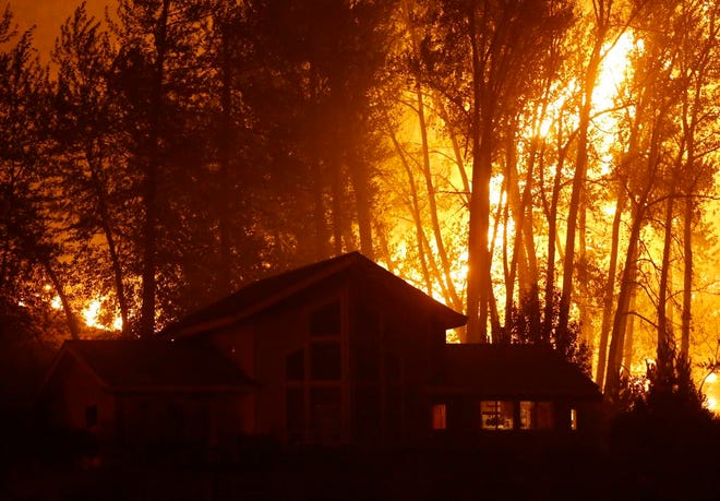A wildfire burns behind a home on Twisp River Road, Thursday, Aug. 20, 2015 in Twisp, Wash. Authorities on Wednesday afternoon urged people in the north-central Washington town to evacuate because of a fast-moving wildfire. (AP Photo/Ted S. Warren)