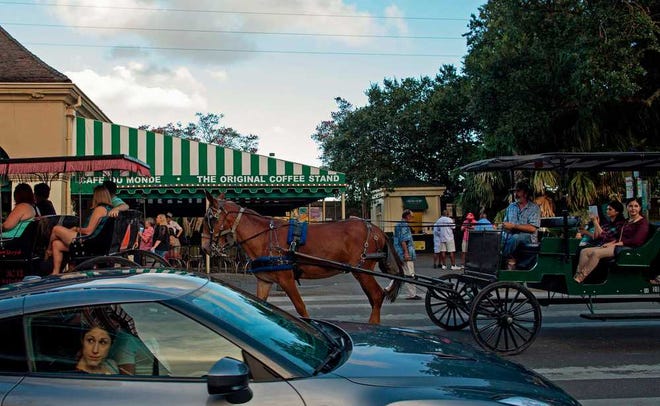 Tourists in cars and horse drawn buggies pass the Cafe du Monde in the French Quarter of New Orleans, Saturday, Aug. 15, 2015. New Orleans is nearly three centuries old, mixing African-American, French, Spanish and Caribbean traditions to create unique forms of music, food and culture found nowhere else in America. (AP Photo/Max Becherer)