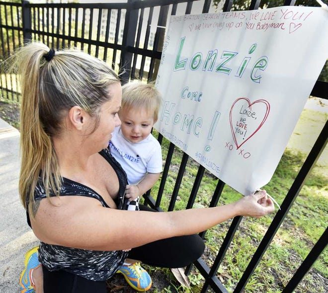 Will.Dickey@jacksonville.com--08/22/15--Kellie Ann Kelleher and her son Jackson, 10 months, put up a sign as people gathered for a search for missing toddler Lonzie Barton Saturday, August 22, 2015 at the John Lowe Boat Ramp at Goodby's Lake in Jacksonville, Florida. Kelleher also brought snacks and drinks for the searchers. (The Florida Times-Union, Will Dickey)