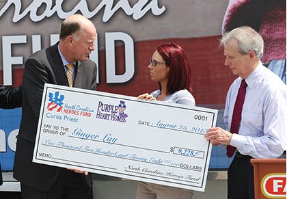 David Hayden, chairman of the North Carolina Heroes Fund, shakes hands with Ginger Lay, the recipient of a check to defray home repair costs as Congressman Walter B. Jones looks on during a ceremony held at Lejeune Memorial Gardens, Tuesday morning.