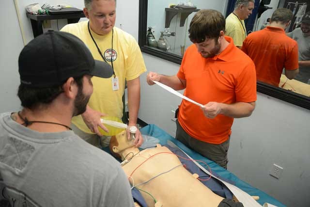 From left, Sean Dailey, Johnny West and Sam Hawke read vials and apply medical care as they learn Emergency Services training on a patient simulator Wednesday at Lenoir Community College.