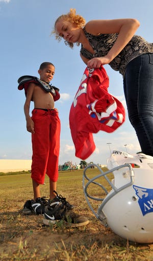 Tina Anderson helps her son Carmello Anderson, 7, put his pads and jersey on as he waits for his first football game ever where he will play with his team the RV Patriots. Carmello has cerebral palsy which limits his abilities.