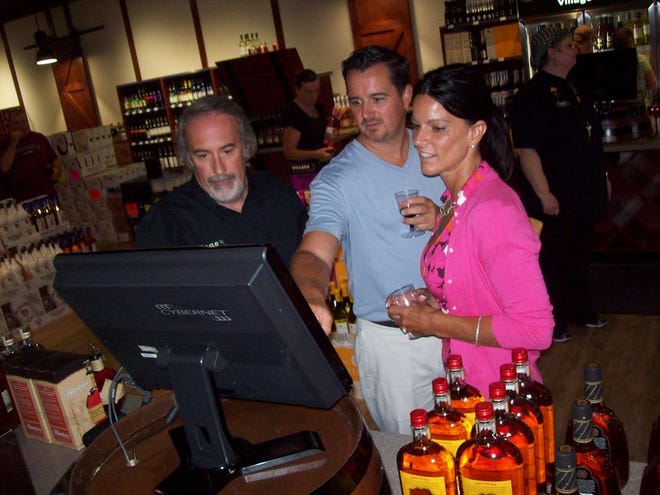 Village Wine & Spirits owner Dave Vantine, left, shows the exclusive vinopedia computer to guests Dean DeRoberts, center, and Linda DeMuro of Fayetteville during the Hamilton store’s grand re-opening gala on Aug. 29.