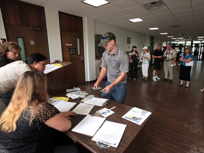 Chris Tenney, center, puts money down on the property he bid on during a foreclosure sale facilitated by, from left to right, Supervisor of Civil Division Julia Rogers, Deputy Clerk Rebecca Delarosa and Deputy Clerk Lori Hardee in the lobby of the Alachua County Courthouse in Gainesville on Aug. 27.