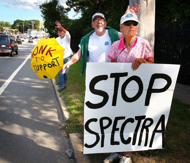 Among those holding signs against a compressor station in the Fore River are are: Dottie Anderson, foreground, and Tom Pendergast, both of Weymouth and John Gauley, of Hingham, holding umbrella, Friday, Aug. 28, 2015.