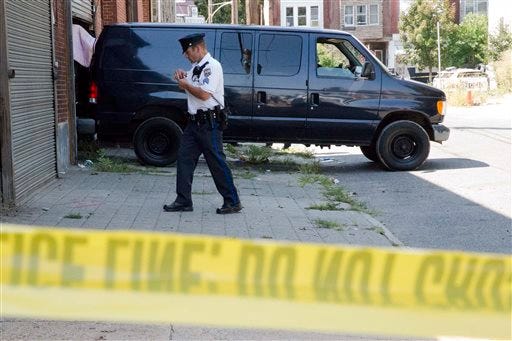 An officer walks in front of a van where bodies are being loaded from a building police say is owned owned by the nearby Powell Funeral Home, Tuesday, Aug. 25, 2015, in Philadelphia. Philadelphia police and city health officials are investigating the discovery of three decomposing bodies in the building owned by a nearby funeral home. Officers were called to the building late Tuesday morning in the Strawberry Mansion neighborhood in north Philadelphia after neighbors reported a foul odor. (AP Photo/Matt Rourke)