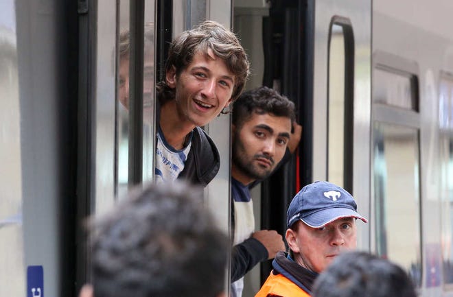 Migrants smile as they board a train to Salzburg at the Westbahnhof station in Vienna, Austria, Sunday, Sept. 6, 2015. Thousands of Arab and Asian asylum seekers surged across Hungary's western border into Austria and Germany following the latest erratic policy turn by Hungary's immigrant-averse government. (AP Photo/Ronald Zak)