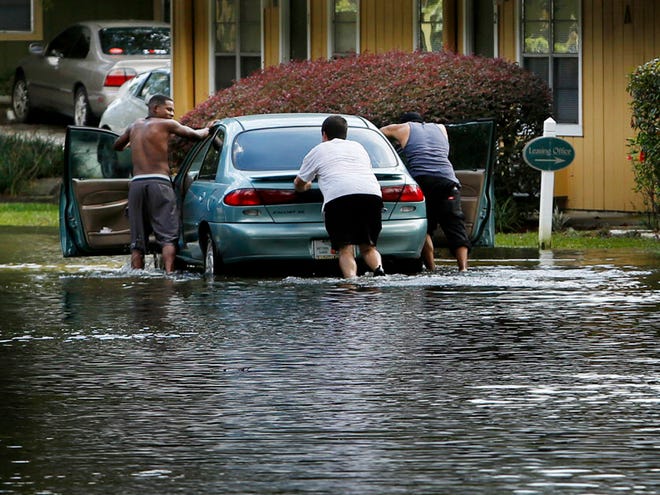 A motorist is helped by a passerby and his passenger after stalling his car while driving through flood waters at the entrance to Hidden Village apartments Tuesday, September 8, 2015.