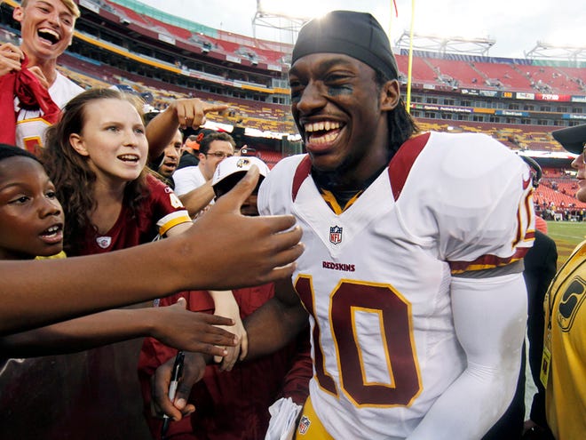 In This Aug. 25, 2012, file photo, Washington Redskins quarterback Robert Griffin III smiles as he greets fans after an NFL preseason football game against the Indianapolis Colts in Landover, Md. Griffin and Indianapolis Colts quarterback Andrew Luck were drafted back-to-back as No. 1 and 2.