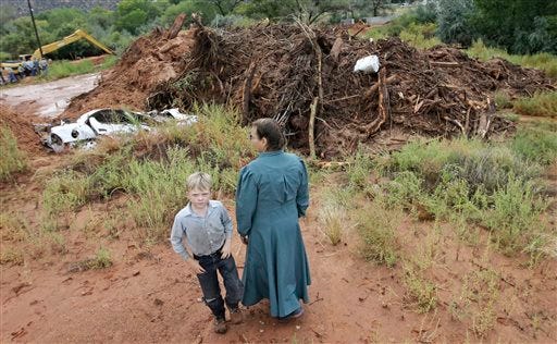 People look over debris and the remains of a car following a flash flood Tuesday, Sept. 15, 2015, in Colorado City, Ariz. Officials say the bodies of two people killed in flash flooding in southern Utah were recovered in Arizona about two and a half miles downstream, while the bodies of six others were recovered in Utah.