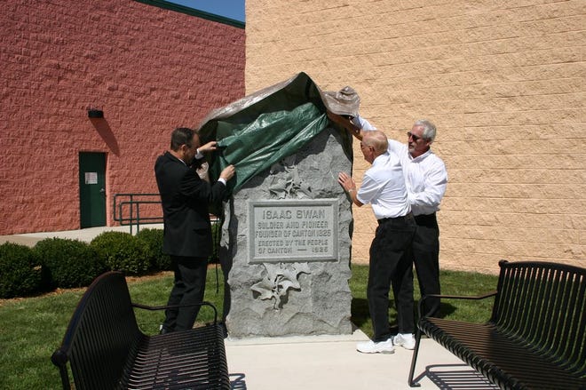 Canton Mayor Jeff Fritz, left, Ray Cleer of the Main Street Design Committee, center, and Jim Murphy of the Cook Group, right, unveil the Centennial Monument in its new home on the square in downtown Canton. The stone, dedicated to Canton founder Isaac Swan, formerly was housed in a remote corner of Greenwood Cemetery until it was relocated earlier this summer.
