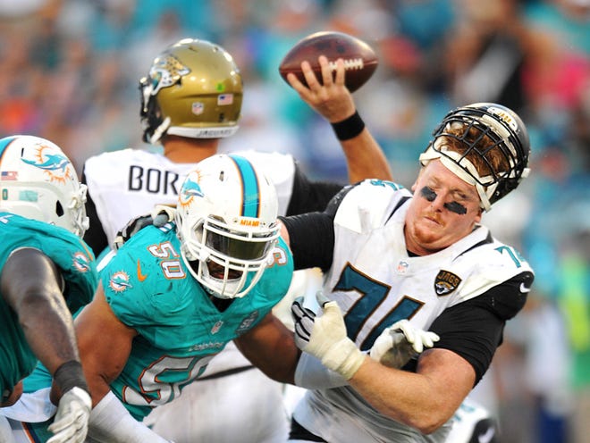 Jaguars offensive tackle Sam Young (74) gets his helmet rearranged while battling with Miami Dolphins defensive end Olivier Vernon (50) in fourth quarter action Sunday, September 20, 2015 at EverBank Field in Jacksonville, Florida. The Jaguars won 23-20.