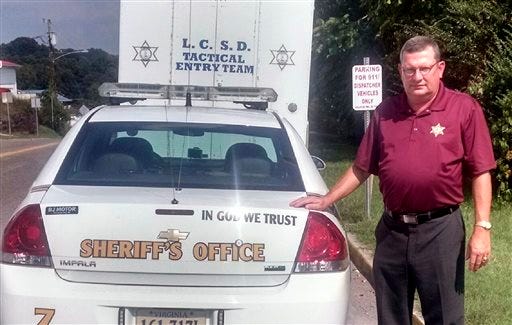 Lee County, Va., Sheriff Gary Parsons stands next to a patrol car that displays an "In God We Trust" decal on Friday, Sept. 4, 2015. Parsons said his office spent a total of $50 to have the decals added to about 25 vehicles. He said many people feel their belief system is being trampled and that adding the phrase is a way of pushing back. But a watchdog group says the decals amount to an illegal government endorsement of religion. (Rex Bailey/Lee County Sheriff's Office via AP)