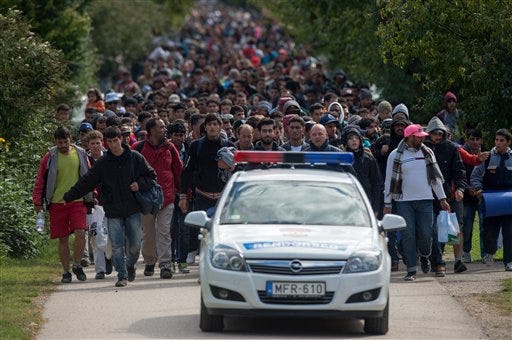 Migrants walk behind a police car in the Hungarian border town of Hegyeshalom toward the border of Austria on Monday Sept. 28, 2015.