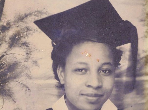 Carrie Newkirk pictured in graduation regalia. She is smiling and has short hair.