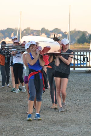 Hingham crew athletes carry their boat back from the water at the end of a recent 5:00 a.m. practice. Pictured (left side of boat, front to back): Lauren Kourafas, Angela Stanley, Grace Galko, Delaney Donnelly, coxswain Lauren Mitchell and (right side of boat, front to back): Hannah English, Hannah Kerber. COURTESY PHOTO/ Dana Donnelly