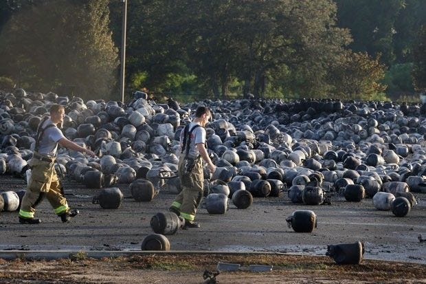 Firefighters walk through an area of exploded propane cylinders in the aftermath of an explosion and fire at the Blue Rhino propane gas plant in Tavares on July 30, 2013.