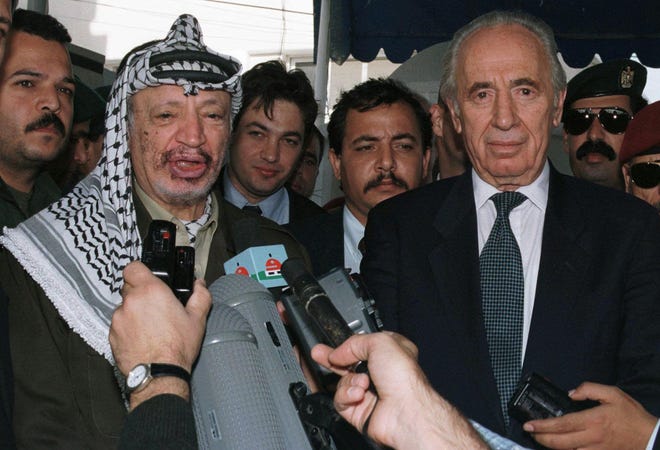 In this 1997 file photo, former Israeli Prime Minister Shimon Peres, right, stands beside Palestinian leader Yasser Arafat as he addresses the media after their meeting at Arafat's office in Gaza City. The Associated Press