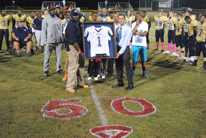 Jones Senior head football coach John Davis, left, and Jones Senior High School Principal Michael White hold a framed jersey in front of the family of Covair Frost and the Trojans’ football team during halftime of Friday’s game against Lejeune. The No. 1 worn by Frost — who starred at JSHS from 2006-08 — was retired by the school Friday night after Frost was shot to death in New Bern earlier this year.