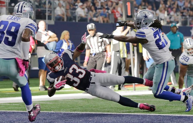New England Patriots' Dion Lewis dives past Dallas Cowboys' J.J. Wilcox, right, to score a touchdown during the second half of an NFL football game, Sunday, Oct. 11, 2015, in Arlington, Texas.