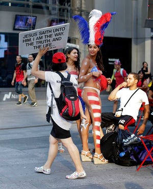 FILE - In this July 28, 2015, file photo, a proselytizer walks by two women clad in thongs and body paint in New York's Times Square. Topless women posing for photos in Times Square are causing headaches for politicians and law enforcement who wish to regulate their presence but have no clear idea how. (AP Photo/Julie Jacobson, File)