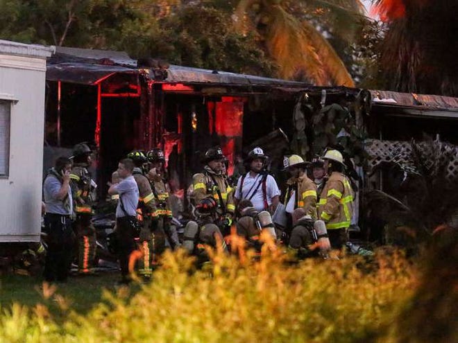 Firefighters stand around after putting out a fire after a small plane crashed into a mobile home park in Lake Worth, Fla.