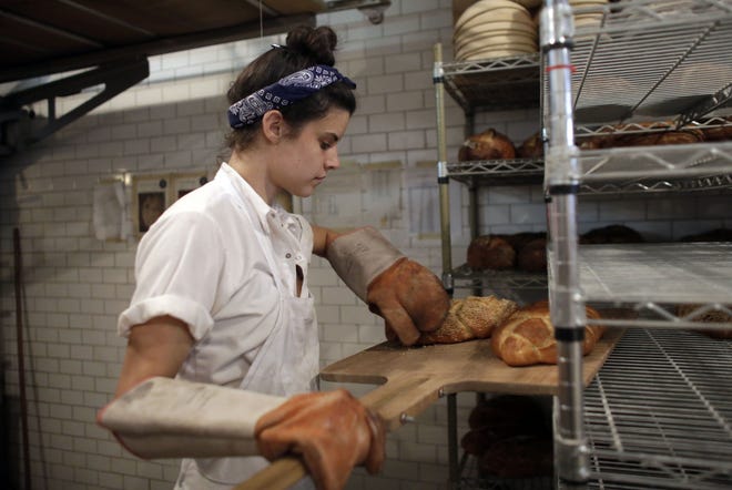Sarah Hinkes places freshly baked bread onto a rack at Zak the Baker in Miami. File Photo/The Associated Press