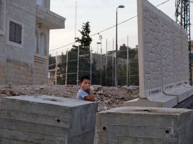 A Palestinian boy stands by concrete barrier between the Arab neighborhood of Jabal Mukaber and the Jewish area of Armon Hanatziv in east Jerusalem, Sunday, Oct. 18, 2015. Israeli police say they have set up a concrete barrier between a Jewish and an Arab neighborhood in east Jerusalem amid soaring tensions. Police spokeswoman Luba Samri says Sunday the slabs were placed there for security reasons, without elaborating. Rocks and firebombs have often been hurled from the Arab area at houses in the Jewish neighborhood.