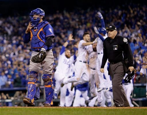 New York Mets catcher Travis d'Arnaud walks off as Kansas City Royals players celebrate Eric Hosmer's game wining sacrifice fly ball during the 14th inning of Game 1 of the Major League Baseball World Series Wednesday, Oct. 28, 2015, in Kansas City, Mo.