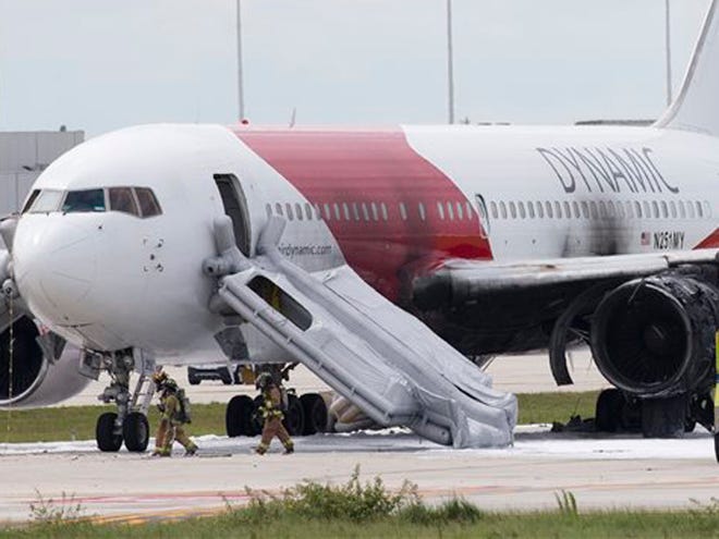 Firefighters walk past a Dynamic Airways Boeing 767, Thursday, Oct. 29, 2015, at Fort Lauderdale/Hollywood International Airport in Dania Beach, Fla. The passenger planes' engine caught fire Thursday as it prepared for takeoff, and passengers had to quickly evacuate on the runway using emergency slides, officials said. The plane was headed to Caracas, Venezuela. (AP Photo/Wilfredo Lee)