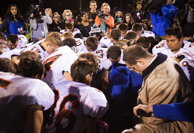 In this Friday, Oct. 16, 2015, file photo, Bremerton High assistant footbal coach Joe Kennedy, center in blue, kneels and prays after his team lost to Centralia in Bremerton, Wash. The coach of a Washington state high school football team who prayed at games despite orders from the school district to stop has been placed on paid administrative. Bremerton School District officials said in a statement late Wednesday, Oct. 28, 2015, that assistant football coach Joe Kennedy's leave was necessitated because of his refusal to comply with district directives that he refrain from engaging in overt, public religious displays on the football field while on duty as a coach.