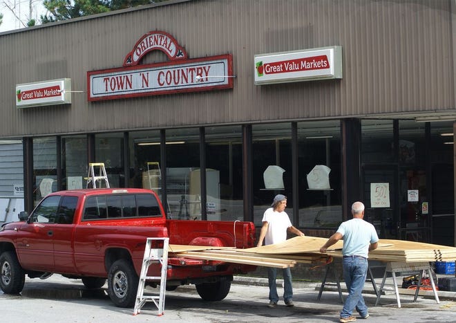 Warren Liles and Matt Bannister unload lumber Thursday afternoon in preparation of boarding up the windows at the Oriental Town N Country grocery, which is closing after more than 40 years.