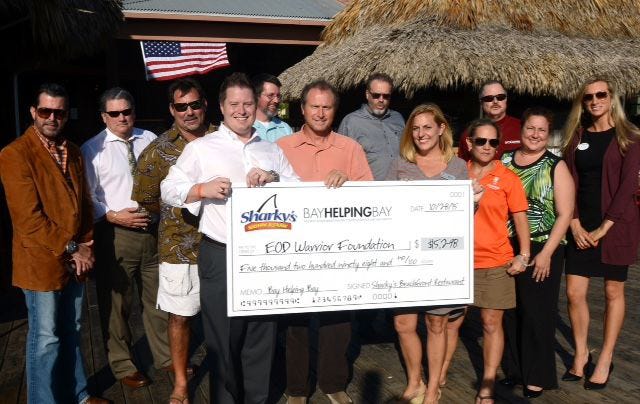 Sharky's Beachfront Restaurant presents a check Wednesday for $5,298 that was raised during the inaugural Bay Helping Bay charity event. Pictured from left are: Stephen Harris, Jeff Storey, Rob Hammer, Grant Wittstruck (holding check), Matt Holbrook (back row), Derrick Bennett (holding check, center), News Herald Publisher Tim Thompson, Kellie Perry, Robin Kurth, John Dunaway, Ava Dixon and Kami Viers.