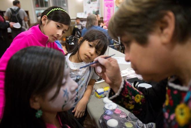 Yuliana Ronses (top left), 9, and Veronica Marquez, 6, watch as Sylvia Landreth paints Diana Robles' face like a skull Monday, Nov. 2, 2015, during a Day of the Dead celebration at the Ethnic Heritage Museum in Rockford. MAX GERSH/STAFF PHOTOGRAPHER/RRSTAR.COM