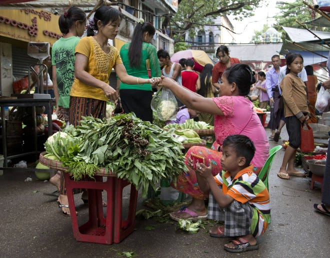 A boy plays on a mobile device as his mother sells vegetables at a street market in Yangon, Myanmar, a country long ruled by the military.