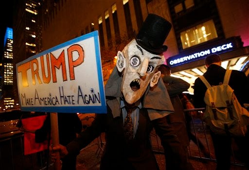A demonstrator dressed in a puppet head with dollar signs in his eyes holds up a sign protesting the scheduled guest appearance of GOP Republican presidential candidate Donald Trump on "Saturday Night Live," Wednesday, Nov. 4, 2015, in New York. -AP Photo/Kathy Willens