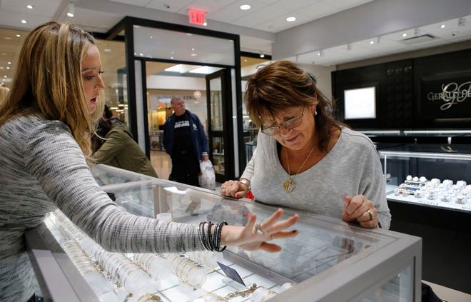 In this Wednesday, Nov. 18, 2015, photo, Alana Fusco, left, an employee at Gerald Peters, a jewelry store owned by Jerry Amerosi at the Staten Island Mall in New York, helps a customer choose a bracelet for her niece. Fusco and other employees of the store will be working Thanksgiving from 6 p.m., until midnight, because the business is in a large mall which could fine the owner as much as $1,000 if he closes on the holiday. (AP Photo/Kathy Willens)