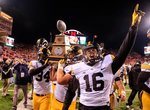 Iowa players, including Nate Meier (34) and Dillon Kidd (16), celebrate with the Heroes Trophy after defeating Nebraska. The Associated Press