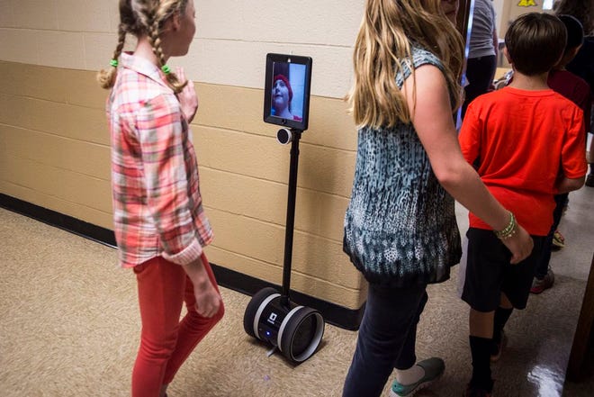 Students walk to class as Peyton Walton practices using a robot system at Poolesville, Md., Elementary School.