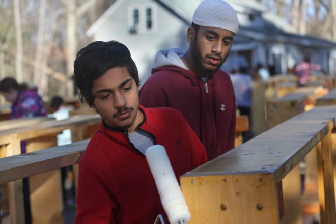 Bilao Ali, left, and Talha Siddiqui, both of the Islamic Center of Framingham, spread sealer on garden boxes Sunday at the Hartford Street Presbyterian Church in Natick. Volunteers from many faiths came together to work on the boxes, which will eventually hold gardens. Daily News and Wicked Local/Lauren McFalls