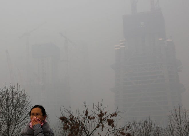 A woman uses a cloth to cover her face from pollutants as she walks past a construction building on a heavily polluted day in Beijing, Monday, Nov. 30, 2015. Beijing on Sunday, Nov. 29, issued its highest smog alert of the year following air pollution in capital city reached hazardous levels as smog engulfed large parts of the country despite efforts to clean up the foul air. (AP Photo/Andy Wong)