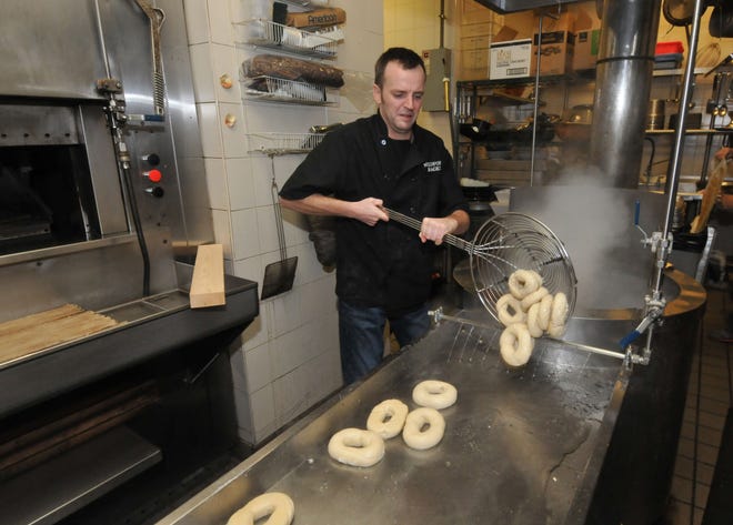 Eric Meile removes bagels from boiling water before adding seeds and baking them.