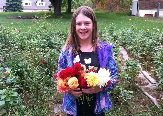 Maggie Hartman, 10, of Hudsonville, poses for a photo with one of the flower bouquets she sells from roadside stands and markets to raise money to buy Christmas presents for area families in need. Hartman is a fifth grade student at ZQuest in Zeeland. Photo courtesy of Jil Hartman.