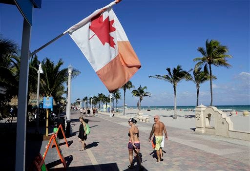 A Canadian flag flies as people walk along the boardwalk in Hollywood, Fla. Visits by the United States' largest supply of international visitors from Canada are expected to be down by 8 percent this year due to the weak Canadian dollar.