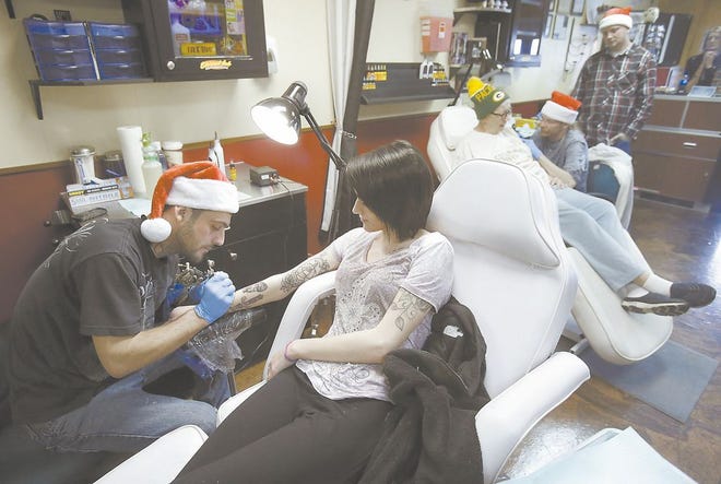 Kenny Brown gives a tattoo to Lexus Ries (foreground) as Marilora Redrick gets a tattoo from Shawn Roberson with Chad Rucker looking on in the background. Reis and Redrick contributed $40 worth of toys to get a tattoo at L.C.C. Tattoo and Supply Company in Canton during a weekend toy drive.