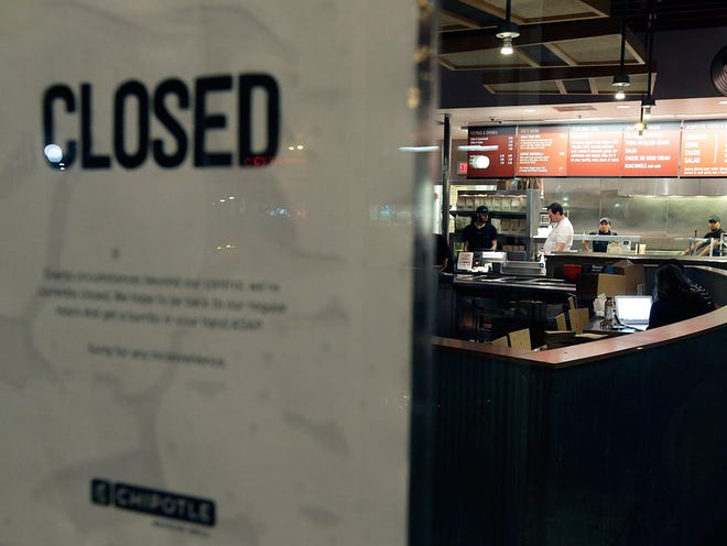 People stand inside a closed Chipotle restaurant on Monday, Dec. 7, 2015, in the Cleveland Circle neighborhood of Boston. Chipotle said late Monday that it closed the restaurant after several students at Boston College, including members of the men's basketball team, reported "gastrointestinal symptoms" after eating at the chain.