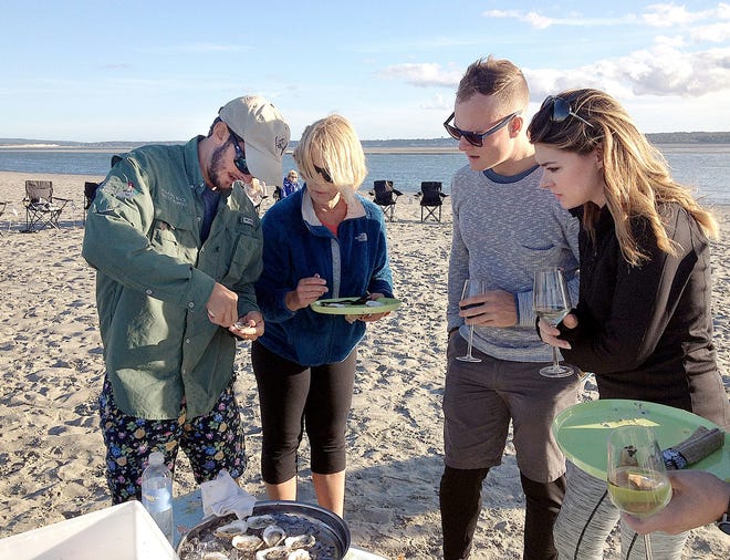 Connor Doyle demonstrates proper oyster-shucking technique to Plymouth resident Dr. Janis Mertz as others look on at a Sept. 27 oyster dinner in Plymouth Bay. Beth Doyle photo/Courtesy of Plymouth Rock Oyster Growers