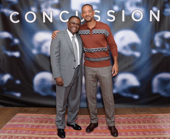 In this Dec. 14, 2015, file photo, Dr. Bennet Omalu, left, and actor Will Smith pose together at the cast photo call for the film "Concussion" at The Crosby Street Hotel in New York. In the trailer for the movie “Concussion,” Will Smith, portraying Omalu, says: “I found a disease that no one has ever seen.” It’s a claim that Omalu, a forensic pathologist, has himself made for years, often even giving a detailed description about how he came to name that disease “chronic traumatic encephalopathy.” But Omalu neither discovered the disease nor named it, according to medical journals and concussion researchers who were interviewed by The Associated Press.